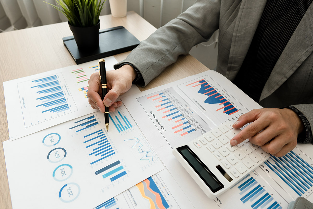 Close-up of a business professional analyzing graphs and charts with a calculator and pen at a desk, representing budget planning and financial strategy.